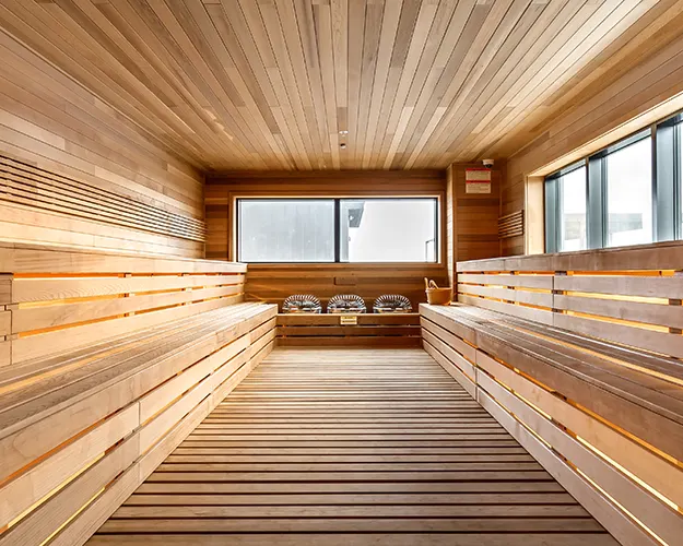 Sauna aus hellem Holz mit Bänken und Saunaofen