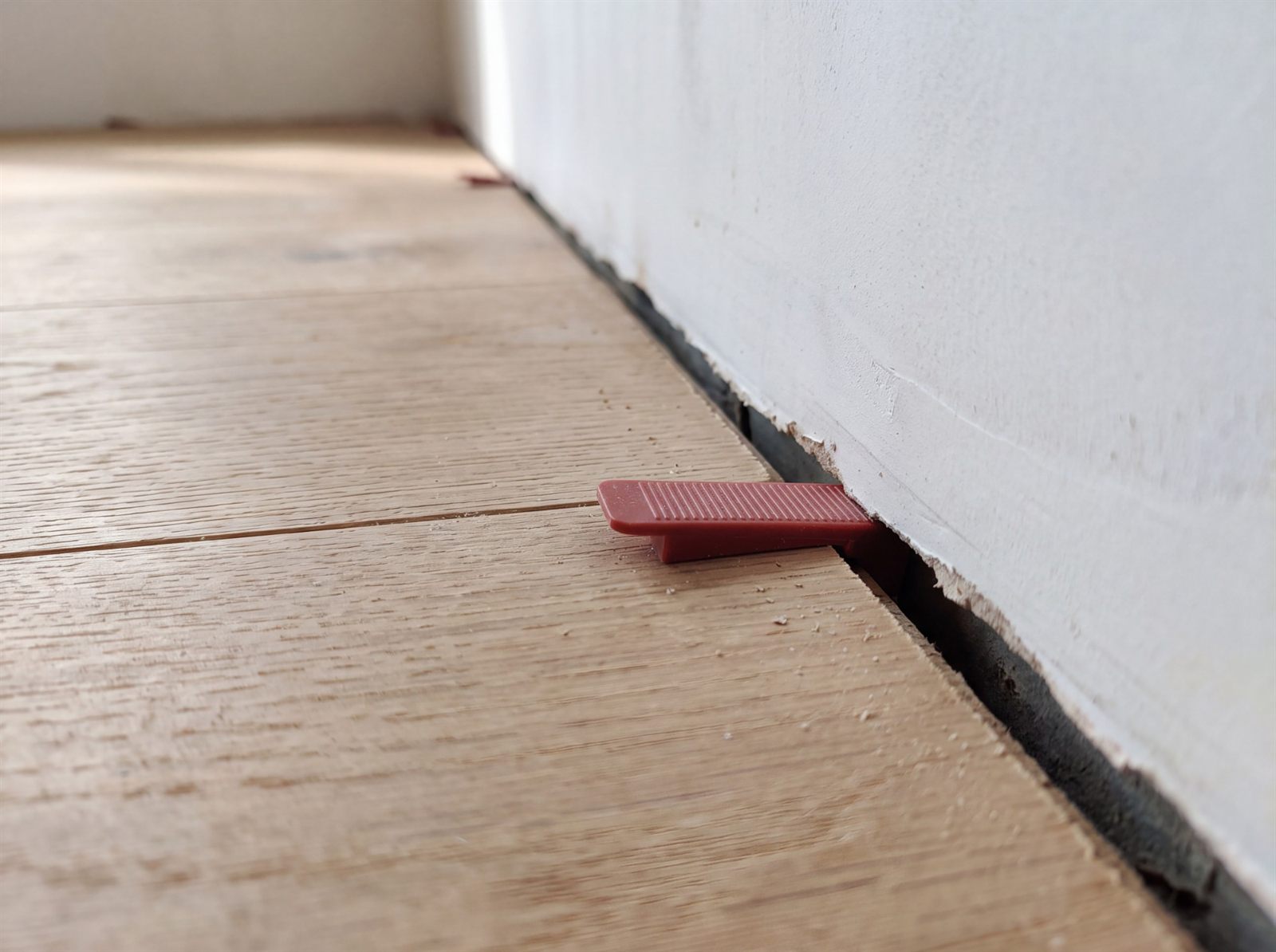 Roter Kunststoffkeil als Abstandshalter zwischen Holzdielen und Wand, die Dehnungsfuge ist sichtbar