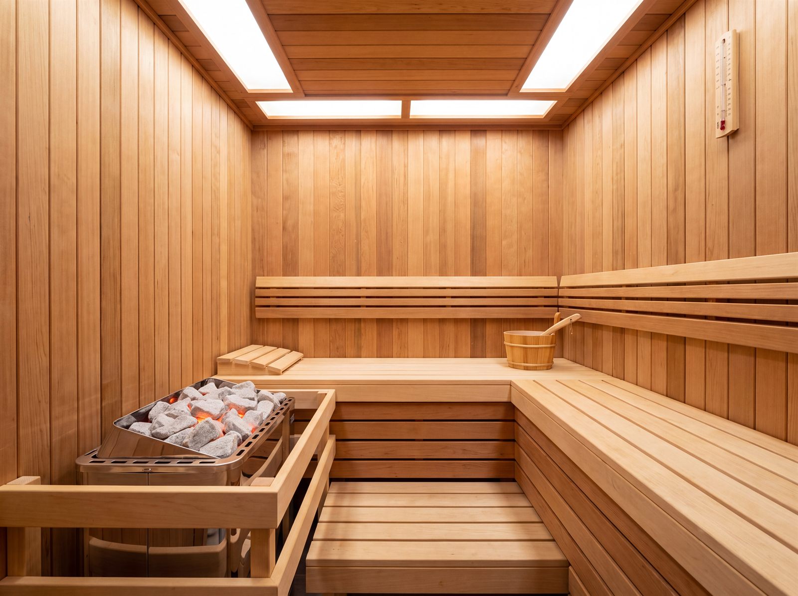 Klassische finnische Sauna mit hellen Holzbänken, Saunaofen mit Steinen und Aufgusskelle