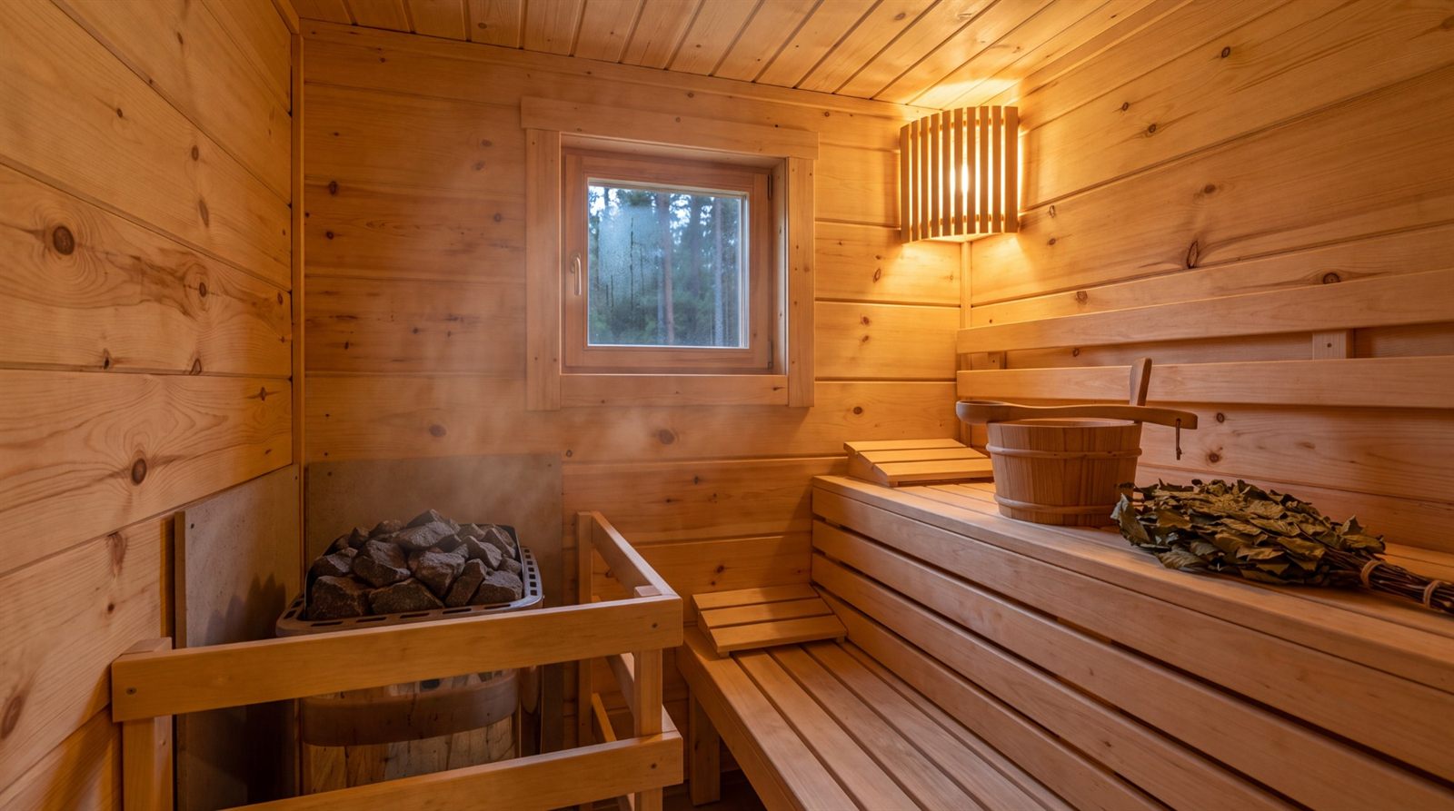 Rustikale Sauna aus Fichte mit sichtbaren Ästen, Saunaofen, Holzeimer und Fenster zum Wald
