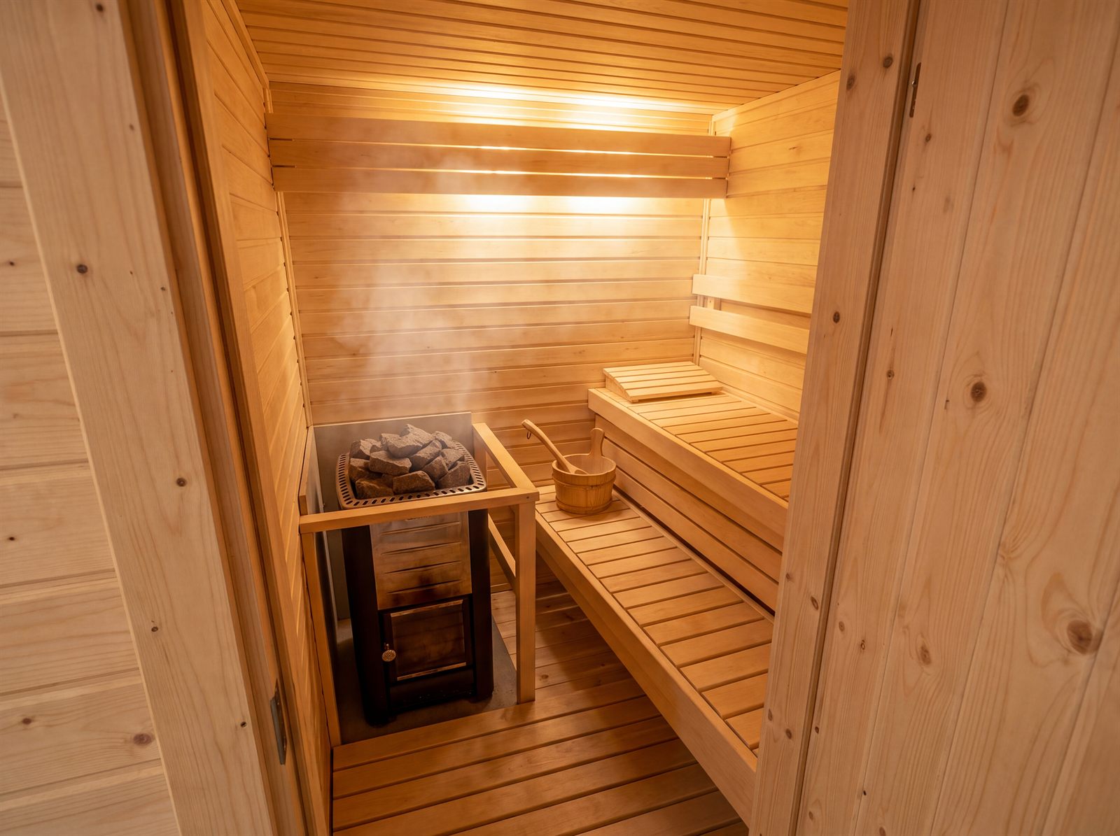 Klassische Holzsauna mit hellen Wandpaneelen, Liegebank und Saunaofen mit Steinen